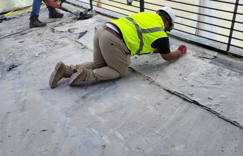 Crew member in hi-vis and a hard hat scraping old flooring material