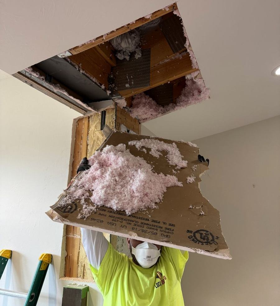 Crew member in a dust mask taking down a section of ceiling