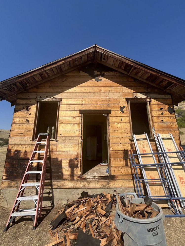 Ranch cabin being taken apart board by board, with reclaimed wood collected in a bin