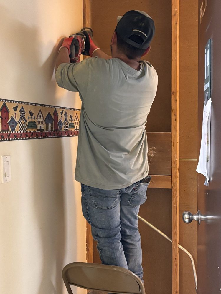 Crew member cutting along a door frame by hand while the wall and wallpaper border beside it stay intact