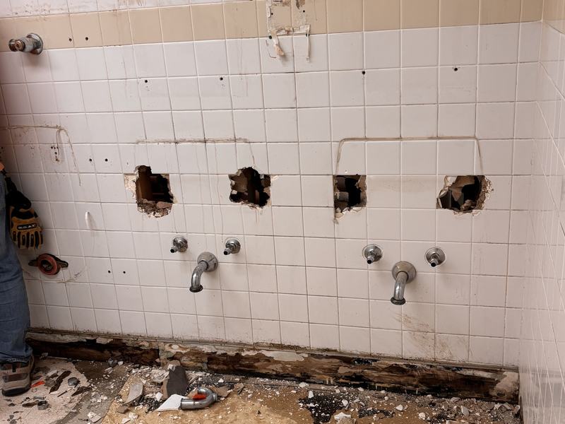 Tile wall with plumbing openings cut and the floor broken out