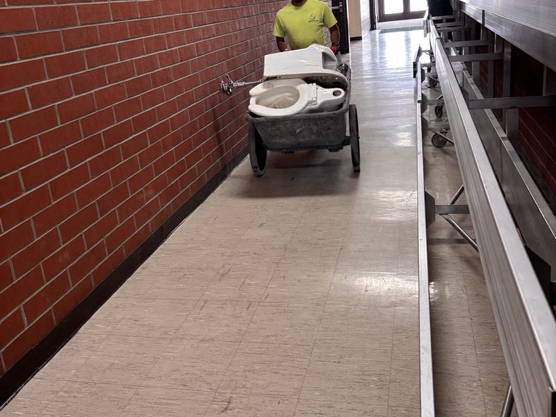Crew member wheeling a cart of demolition debris down a school hallway