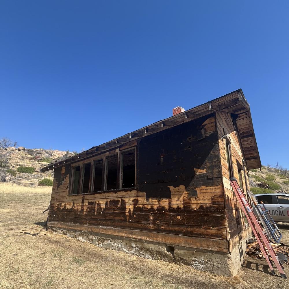 Ranch cabin partly taken apart board by board with a Local Demo truck and ladders beside it